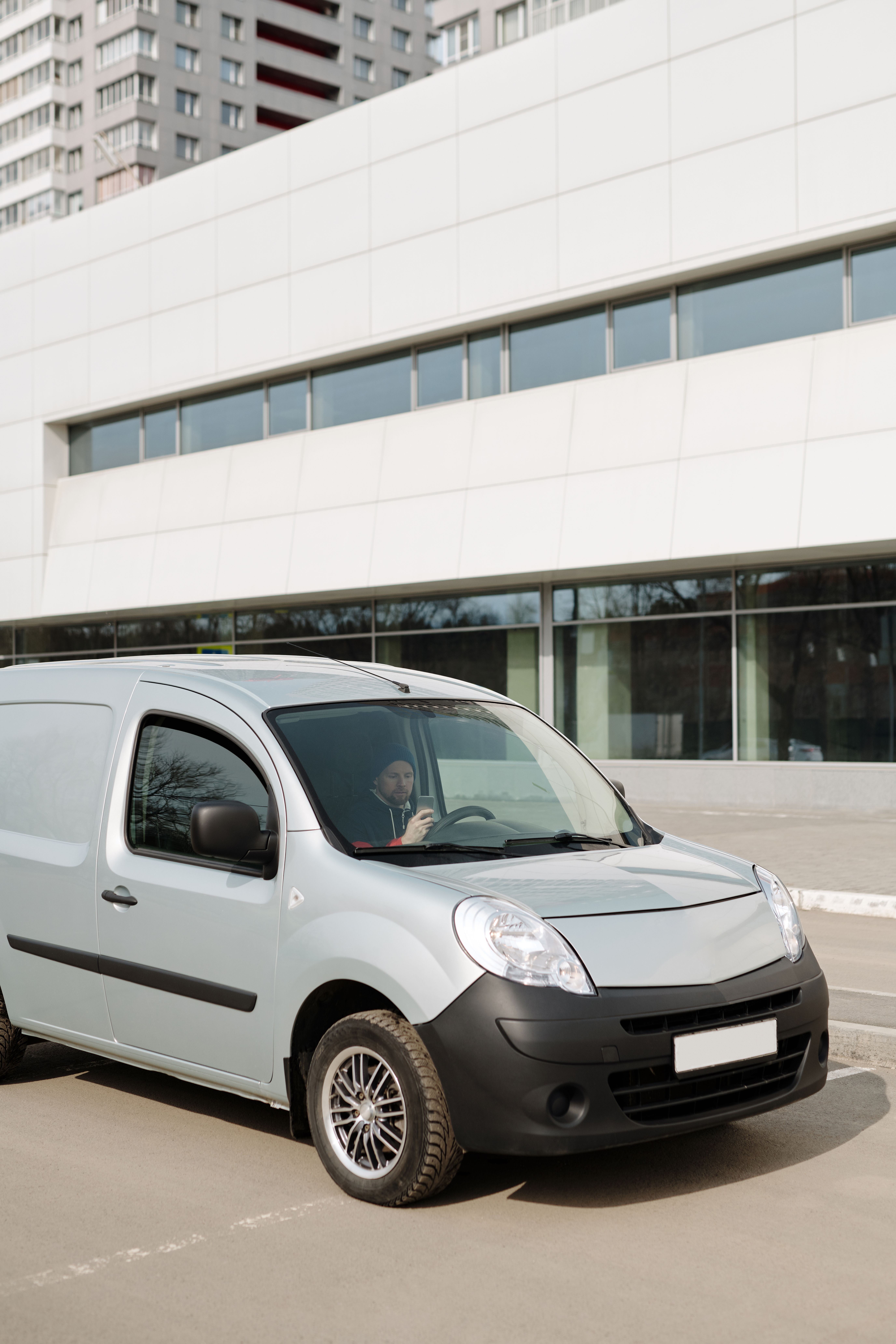 A man in a van parked in front of a modern building, using a smartphone.